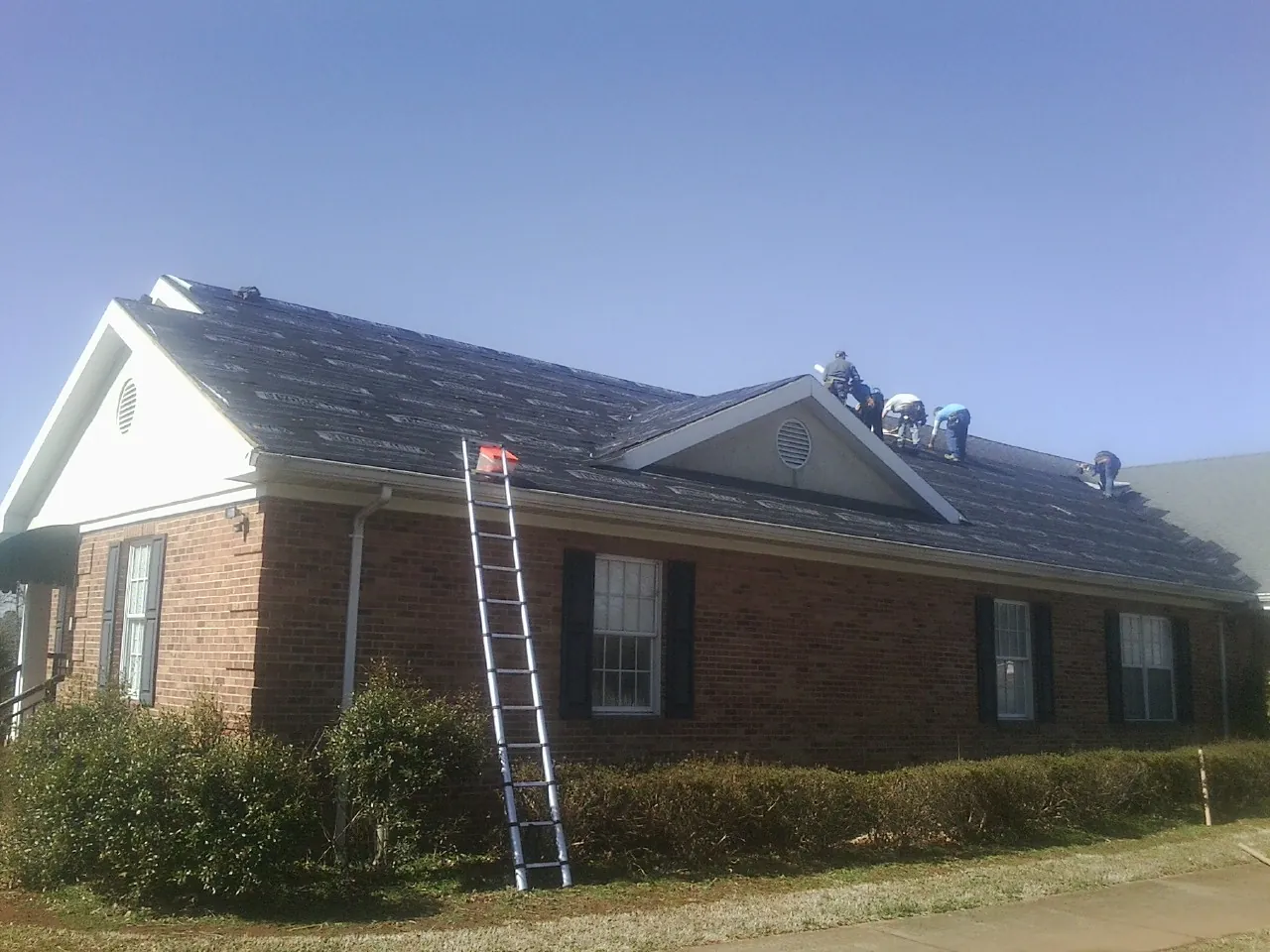 Crew tearing shingles off a brick ranch roof with a ladder set — Emergency Roof Repair work by our crew in Deep River