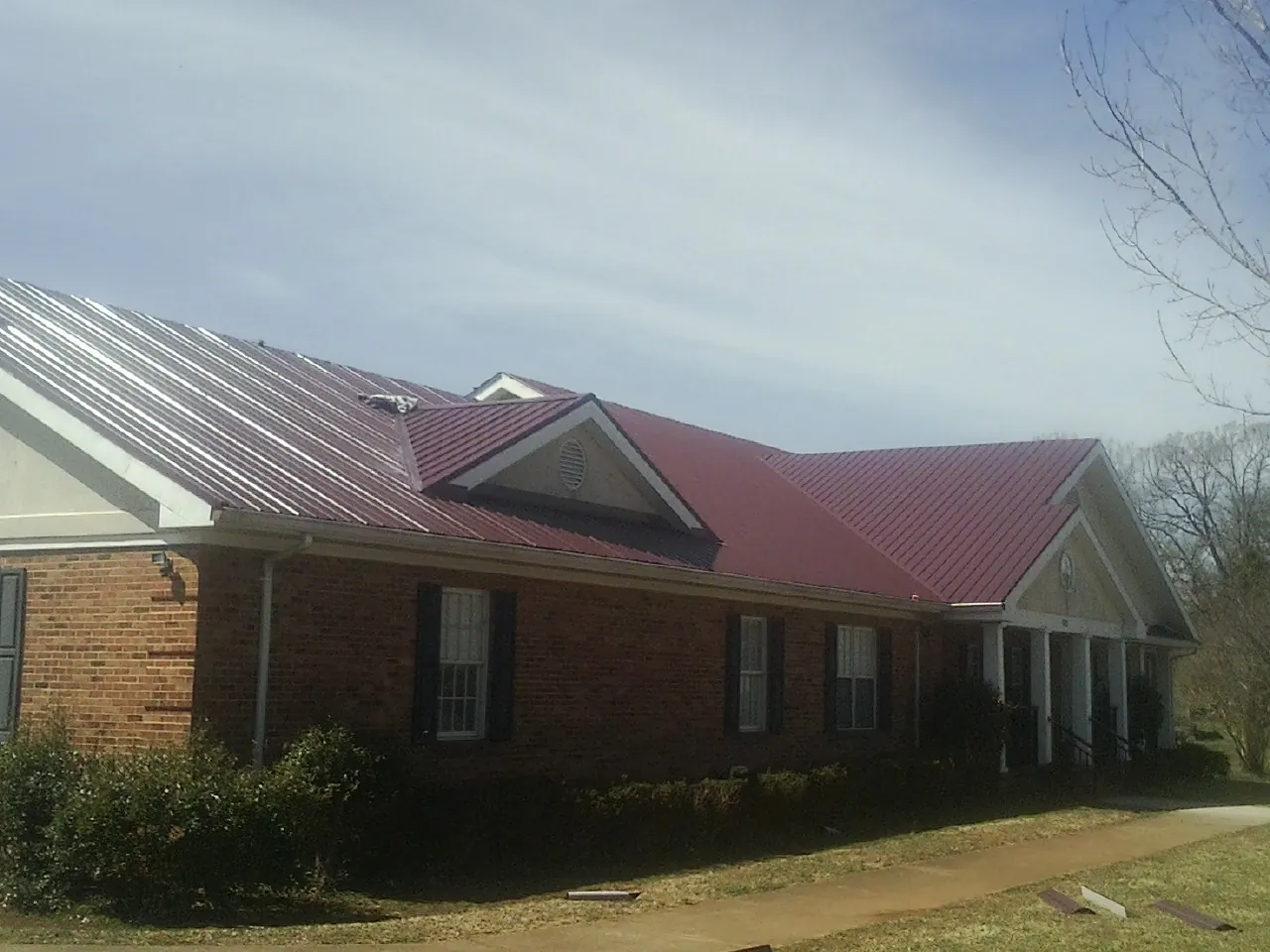 Red metal roof with gabled entries on a long brick building, from a Hail Damage Roof Repair job in Deep River
