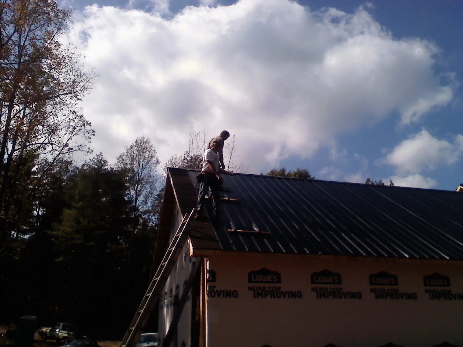 Roofer fastening dark metal panels high against a cloudy sky, from a Roof Inspection job in Deep River